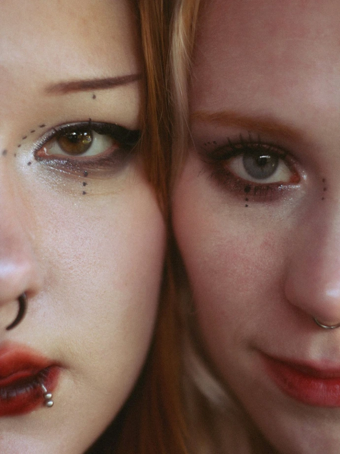 Two women with elaborate makeup and piercings close-up facial features
